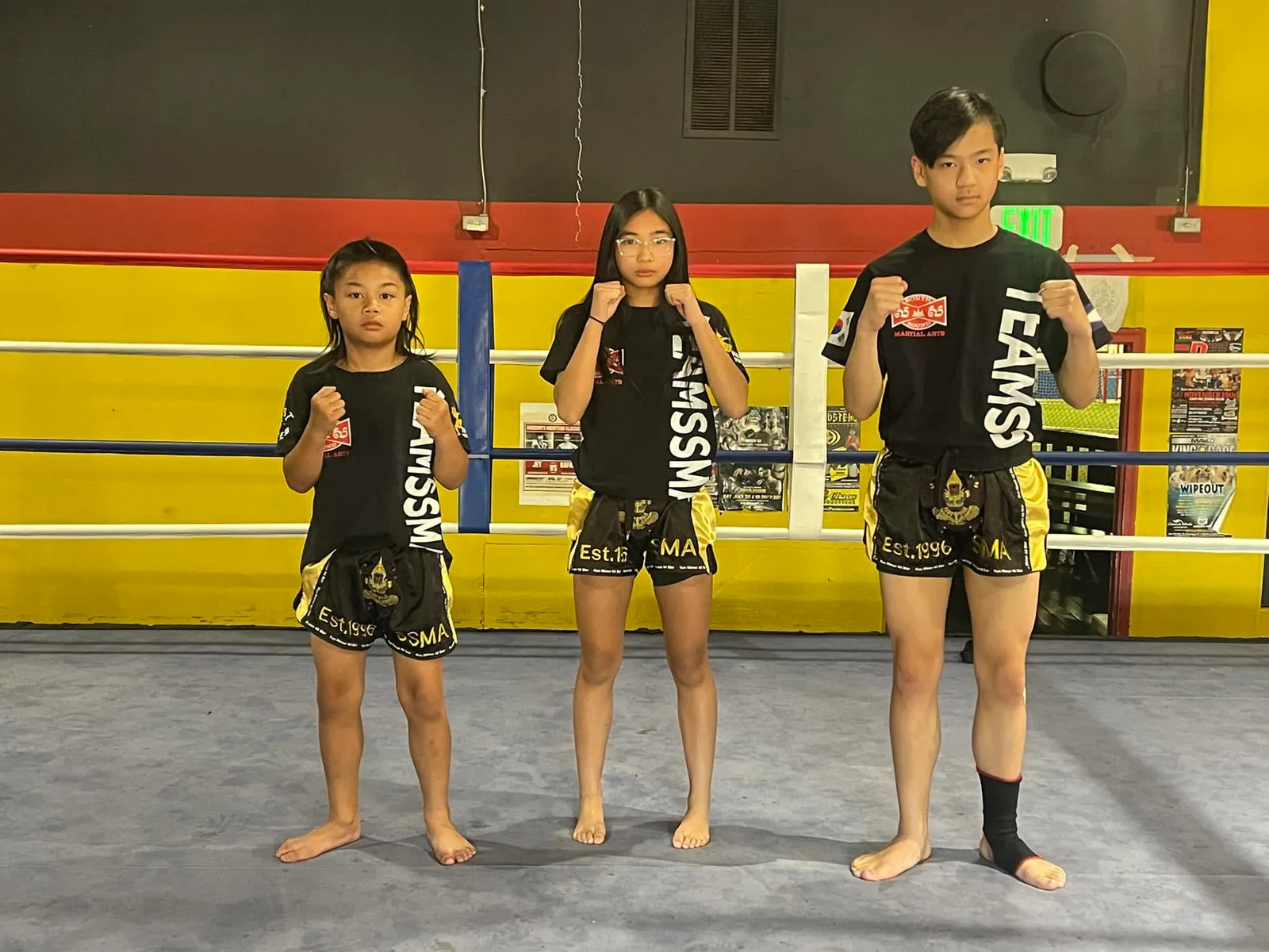 Three young SSMA students standing in the ring in team shirts and Kun Khmer shorts